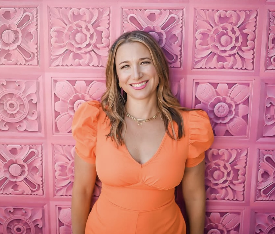Dr. Weiss smiling in an orange dress in front of a pink ornamental tile wall